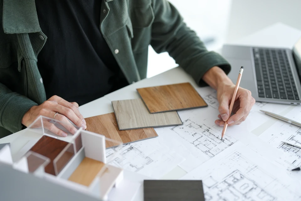Réunion de travail autour d'une table en bois avec deux personnes consultant des nuanciers de matériaux et plans d'architecture