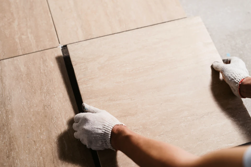 Intérieur en cours de rénovation, artisan carreleur installant du carrelage imitation bois sur chape béton
