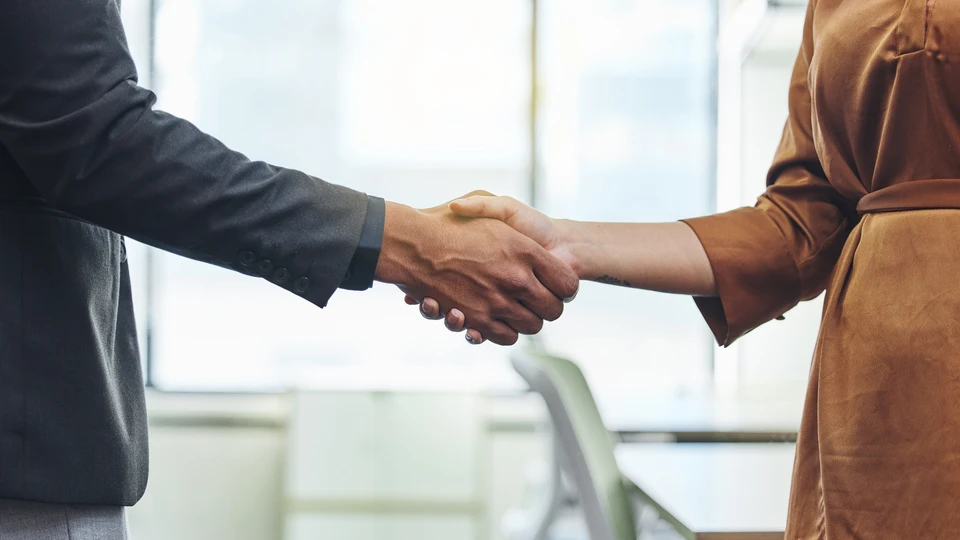 Réunion professionnelle dans bureau moderne avec conseiller en costume-cravate serrant la main d'un client, accompagné d'une femme souriante