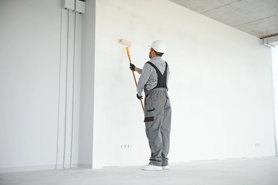 Ouvrier en combinaison grise et casque orange installant des plaques de placo sur un plafond intérieur